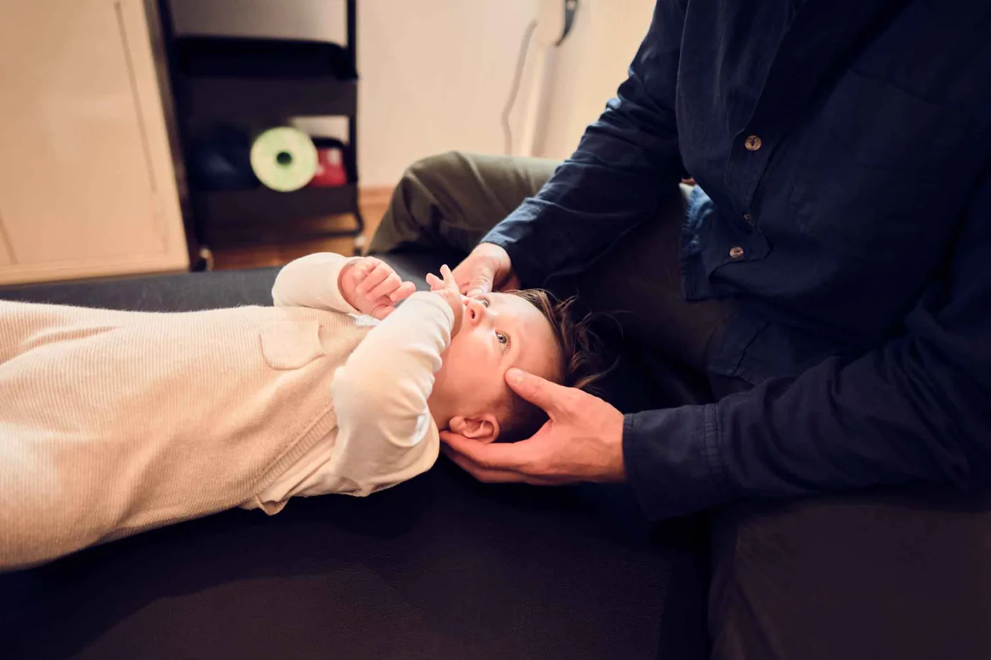 Osteopathische Behandlung eines Säuglings: Die Hände des Behandlers umfassen sanft den Kopf des Babys