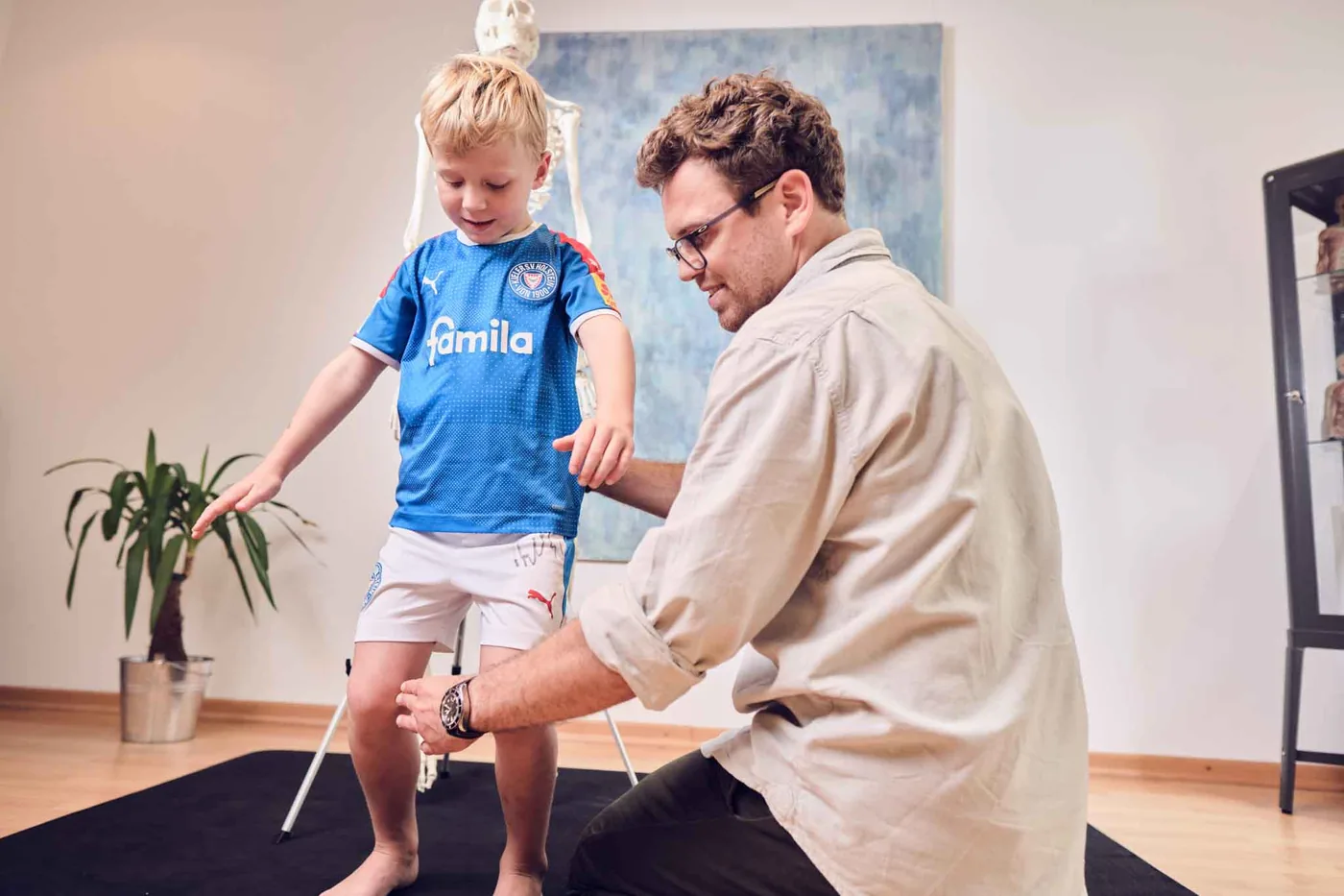 Kontrolle der Beinachsen im Stand: Der Behandler prüft die Knie eines kleinen Jungen